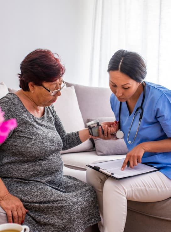 A nurse taking sitting with an older woman and high-risk patient, taking her blood pressure at a transition of care