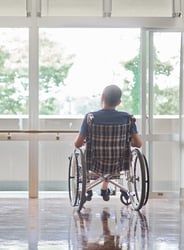 man in wheelchair gazing out bright windows.