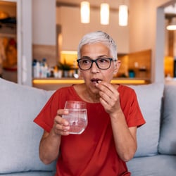 woman in a red shirt holding a glass of water taking medication