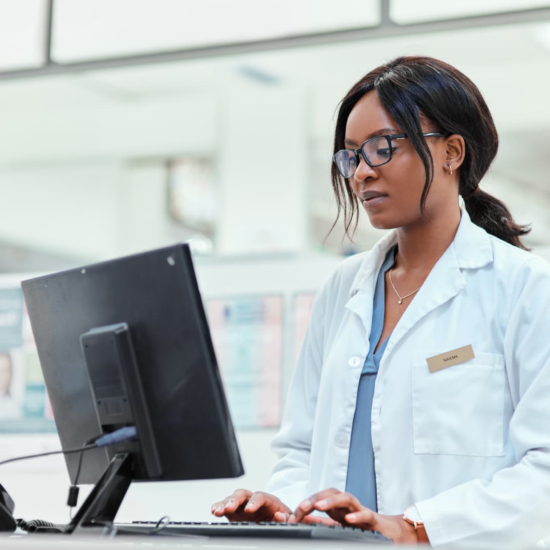 Young female pharmacist standing and working at computer on medication management programs.